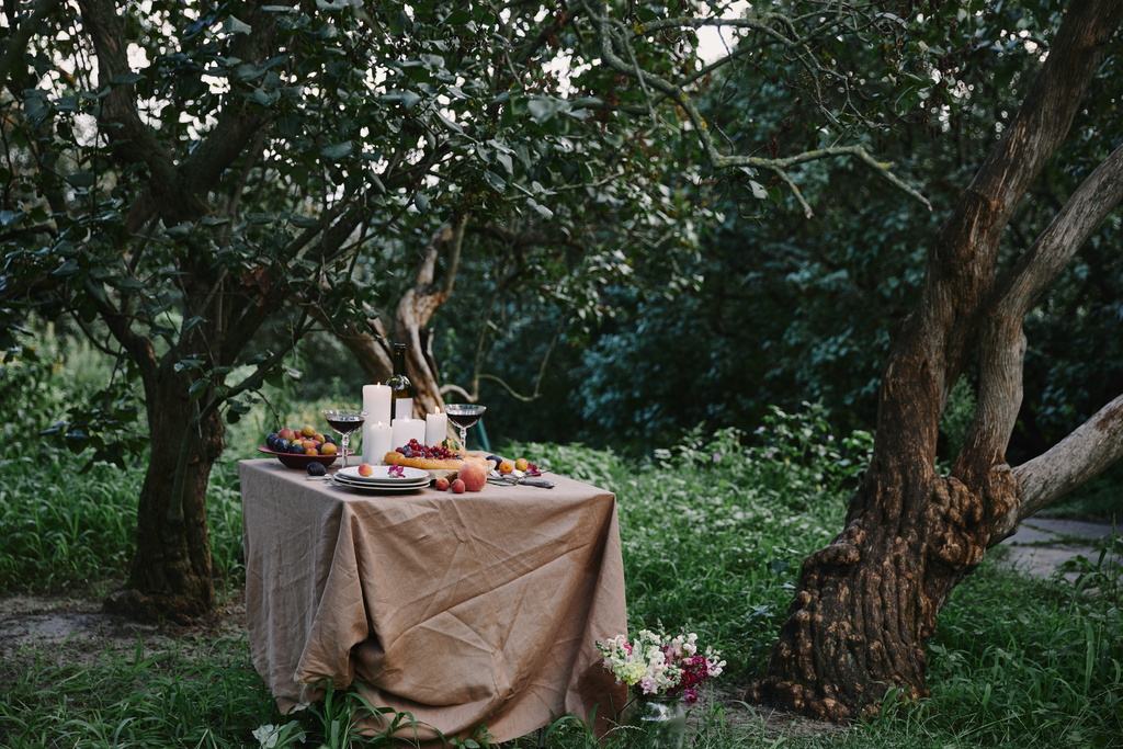 kaarsen, wijn en taart op tafel in de tuin - Foto, afbeelding