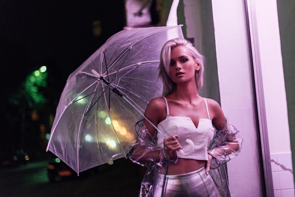 atractiva joven en impermeable transparente con paraguas en la calle por la noche bajo luz rosa
 - Foto, imagen