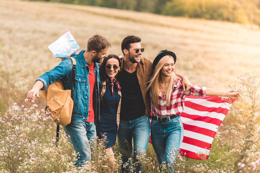 group of smiling young american travellers with flag walking by flower field - Photo, Image