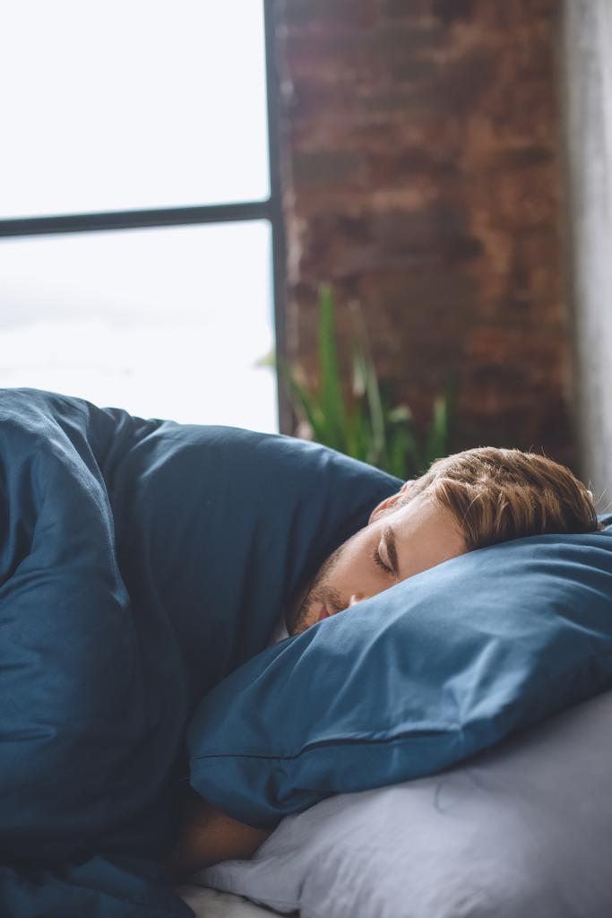 vue rapprochée de jeune bel homme dormant sous la couverture dans son lit à la maison
 - Photo, image