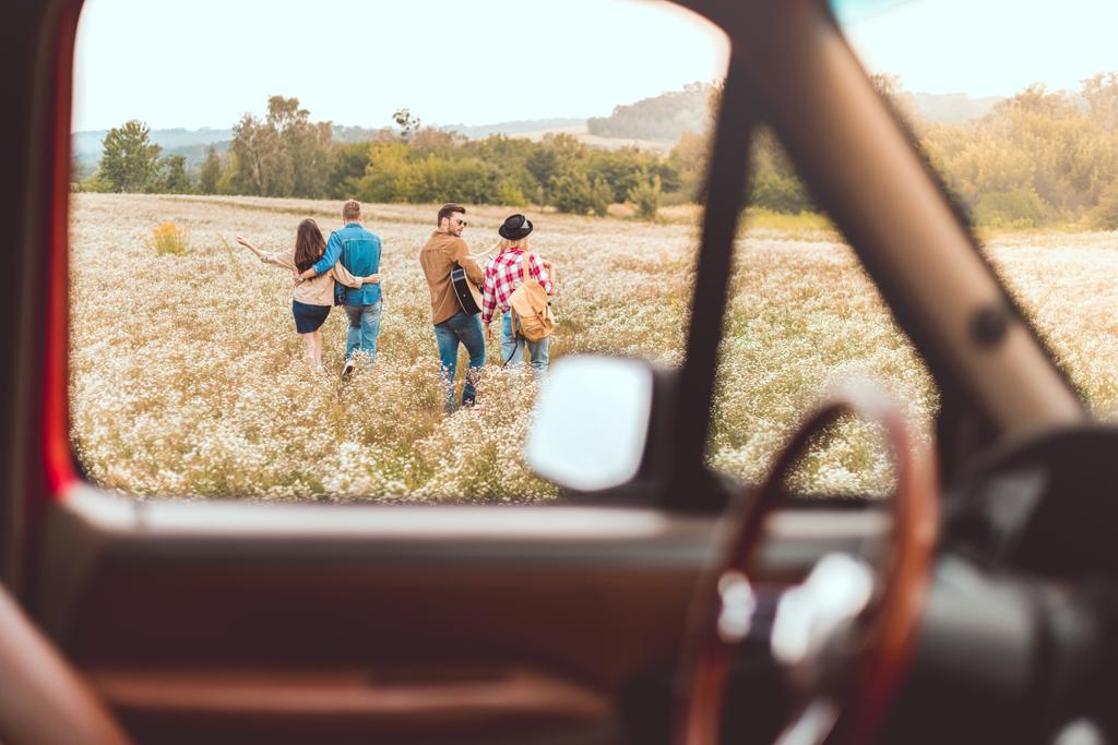 車の旅行中に花畑を歩いて幸せな若い友人のグループで車からの眺め - 写真・画像