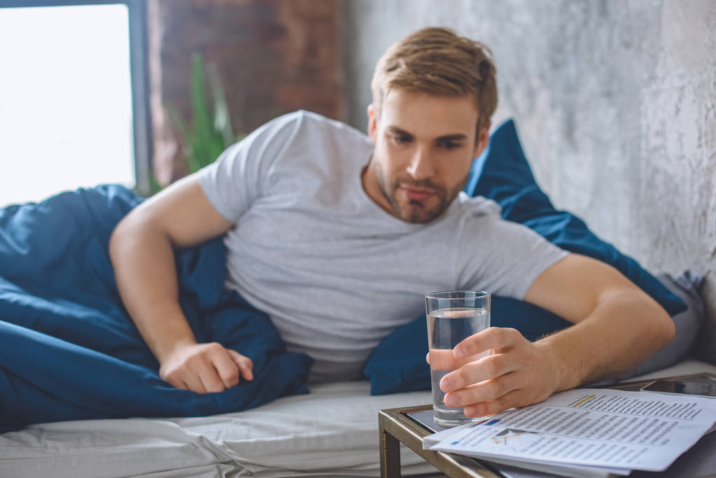 Selektivní fokus mladého muže v posteli s sklenice vody doma - Fotografie, Obrázek
