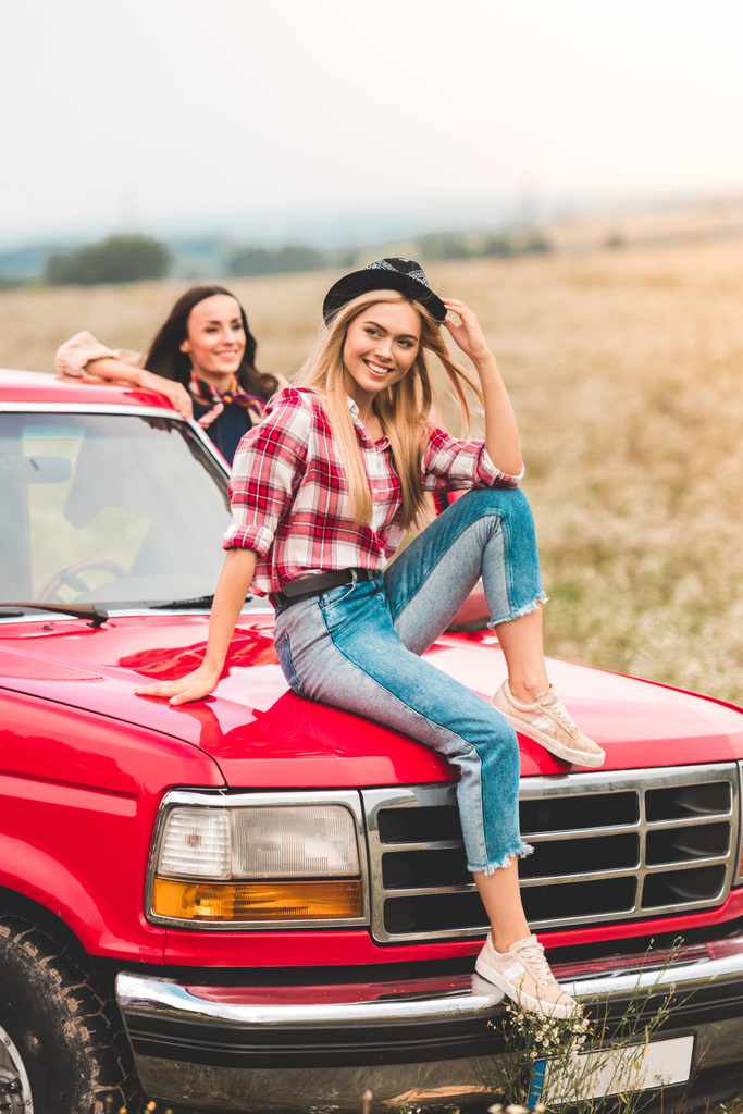 привабливі молоді подружки, які подорожують автомобілем і розслабляються в квітковому полі
 - Фото, зображення