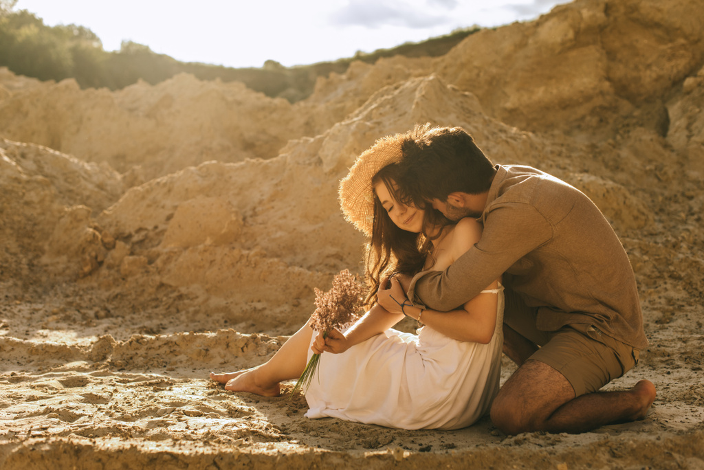 happy man hugging girlfriend in straw hat with floral bouquet in sand canyon - Photo, Image