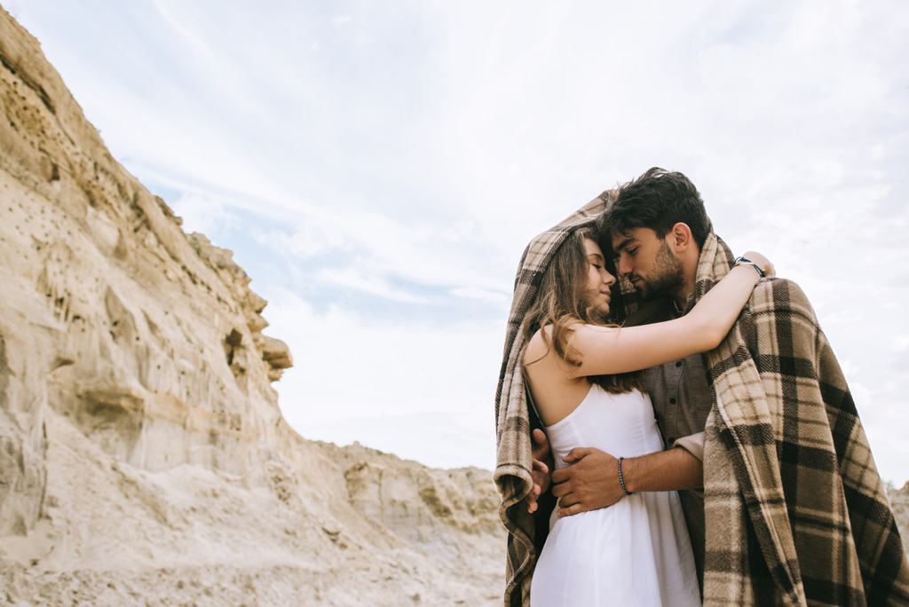 красивая пара влюбленных, обнимающихся под одеялом в песчаном каньоне с облачным небом
 - Фото, изображение