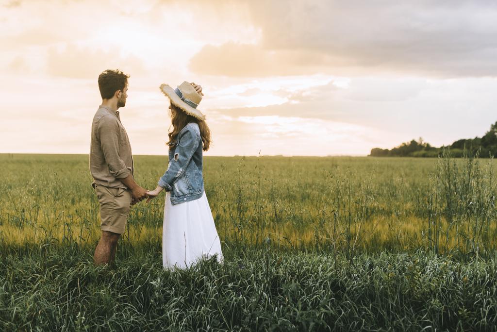 pareja elegante cogida de la mano en el campo verde y mirando el atardecer
 - Foto, Imagen