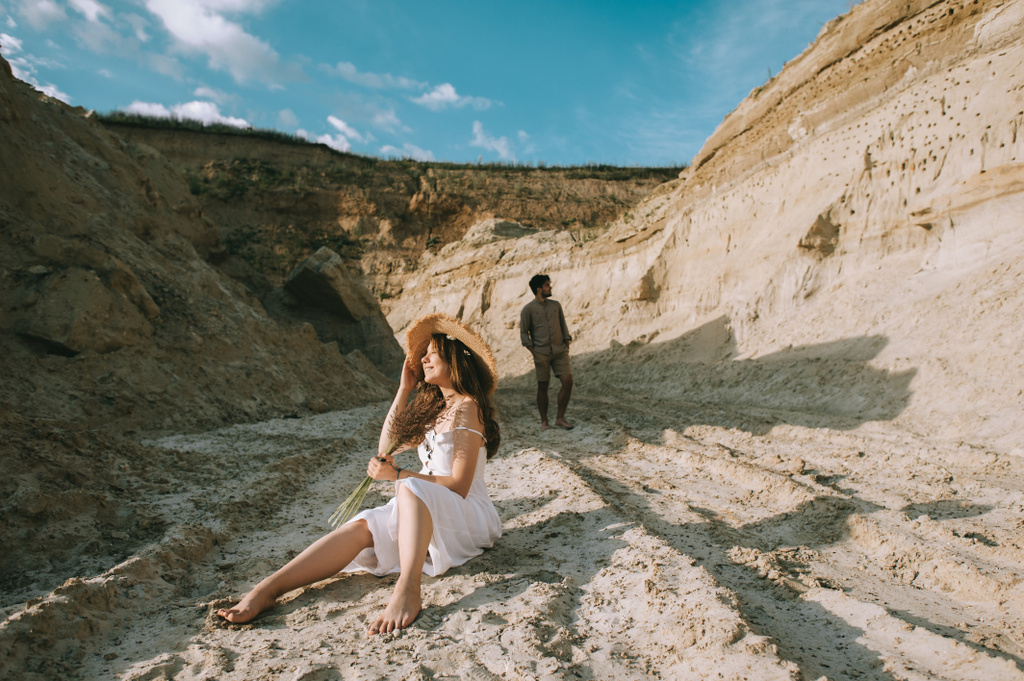 šťastná dívka s květinovým buketem sedí v písku kaňonu s přítelem za - Fotografie, Obrázek