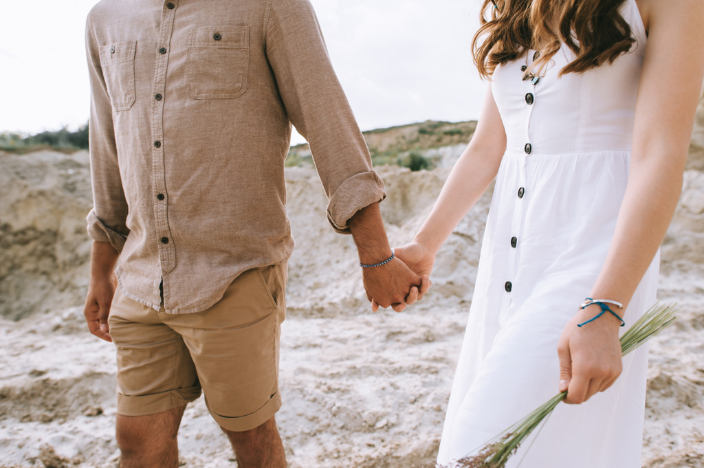 スタイリッシュなカップルは手を繋いでいると砂の渓谷を歩いてのビューをトリミング - 写真・画像