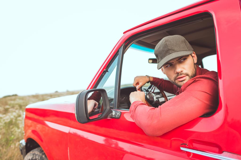 handsome young man driving old red truck in field and looking back - Photo, Image