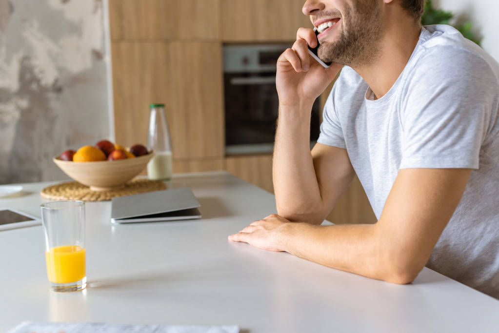 levágott kép mosolygó ember beszél a smartphone a konyhaasztalon, pohár friss gyümölcslé - Fotó, kép