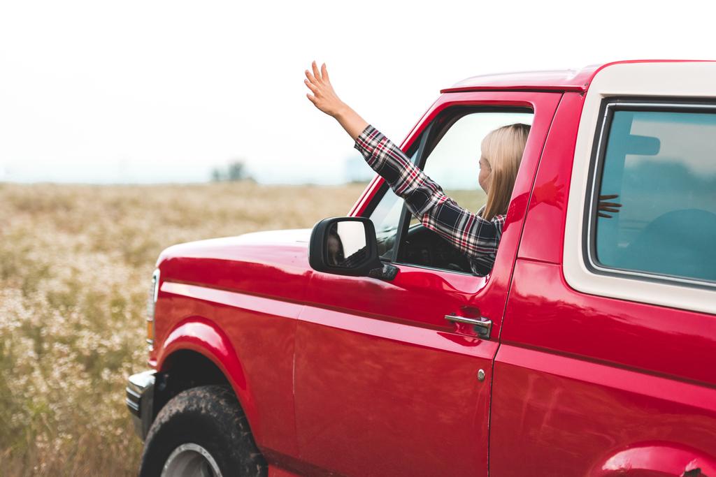 beautiful young woman driving car on flower field and waving - Photo, Image