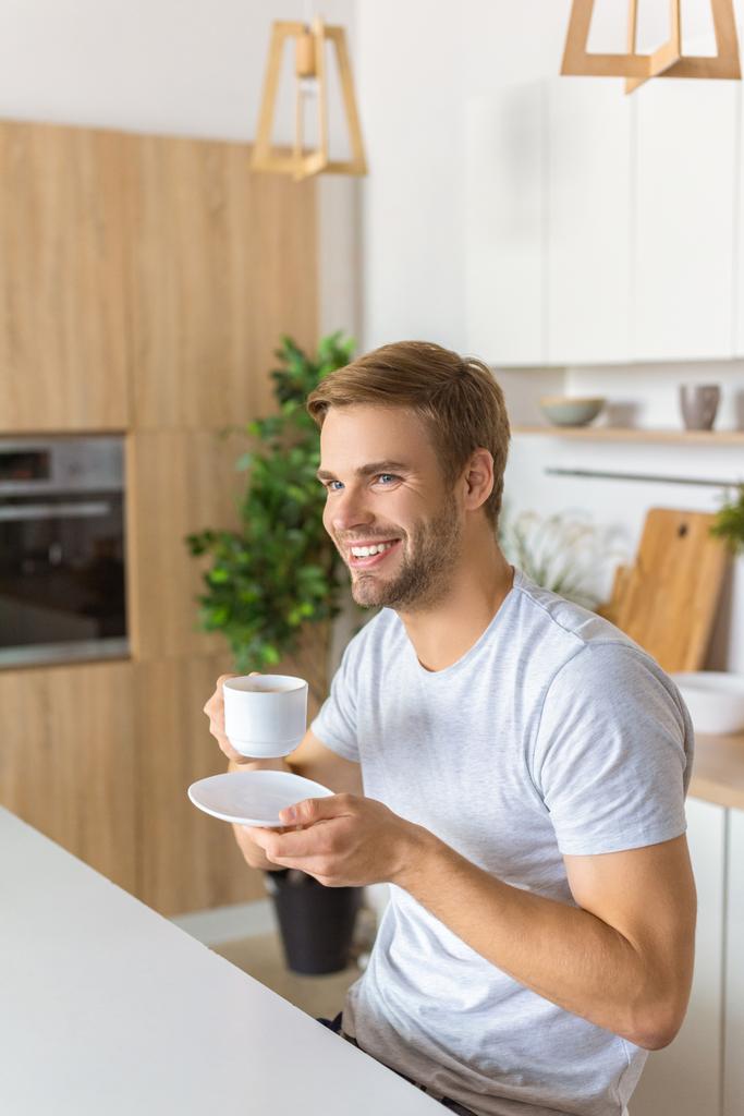 happy young man drinking coffee on breakfast at kitchen table  - Photo, Image
