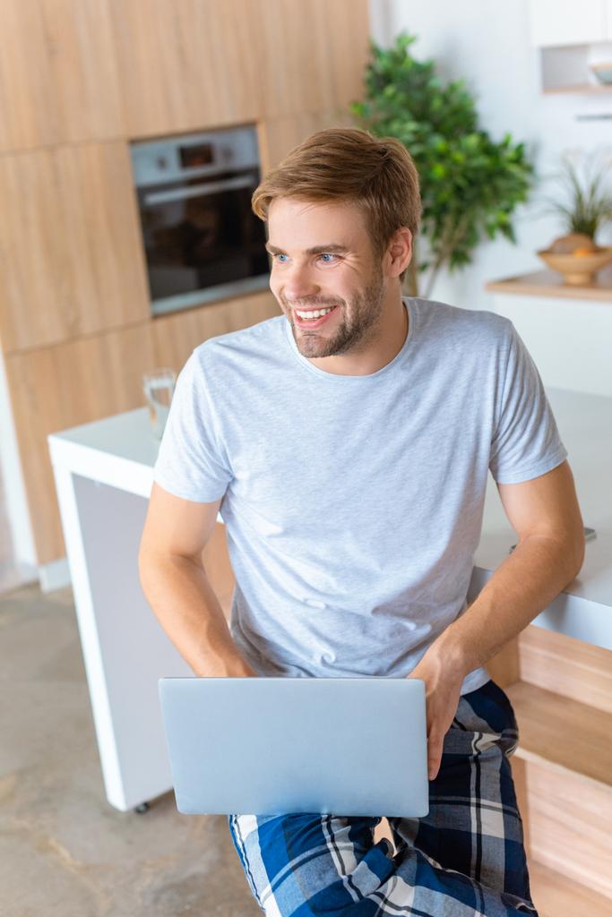 homem bonito feliz usando laptop na cozinha
  - Foto, Imagem