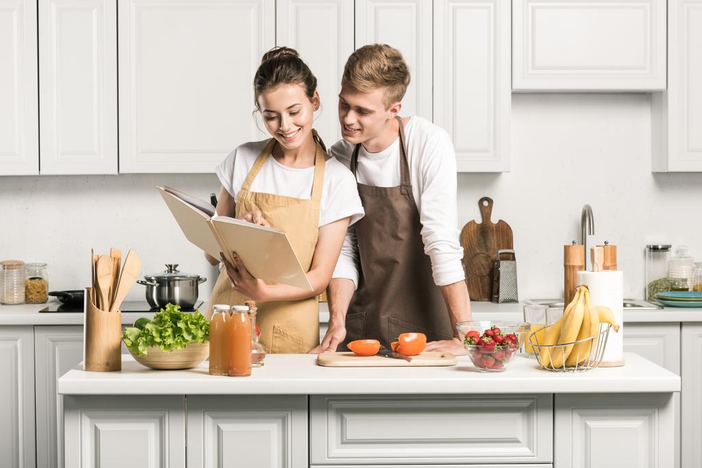 junges Paar kocht Salat und schaut in Küche auf Rezeptbuch  - Foto, Bild