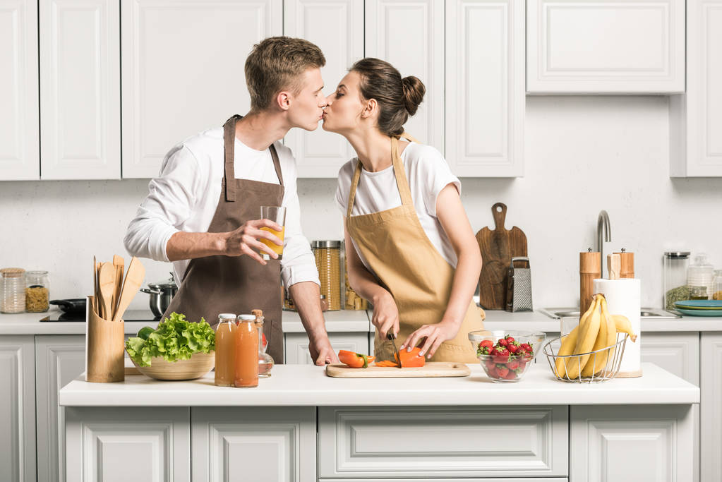 νεαρό ζευγάρι φιλί, ενώ το μαγείρεμα σαλάτα στην κουζίνα - Φωτογραφία, εικόνα