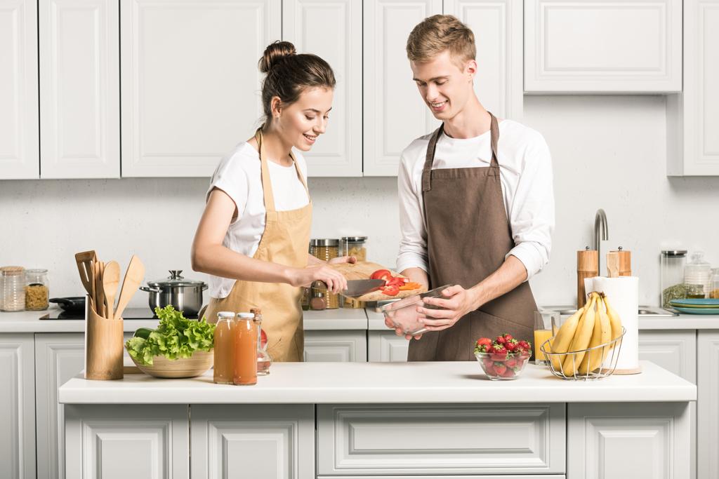 young couple cooking salad and putting vegetables in bowl in kitchen  - Photo, Image