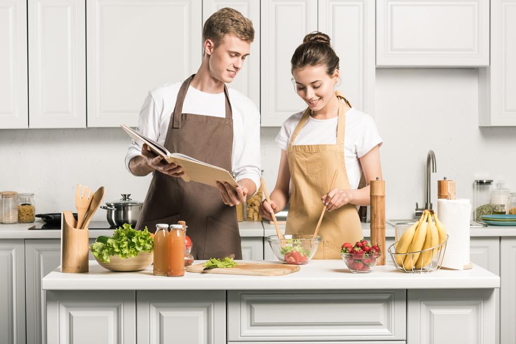 pareja joven cocina ensalada con libro de recetas en la cocina
 - Foto, Imagen