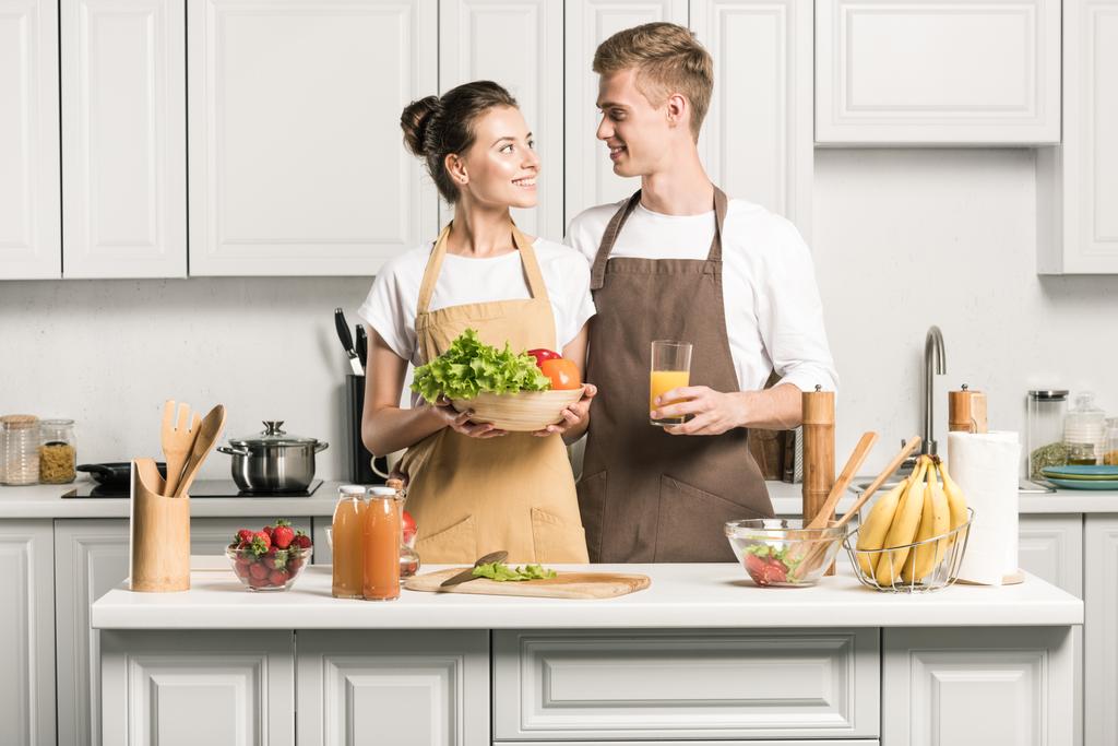 jovem casal segurando legumes e copo de suco na cozinha
 - Foto, Imagem
