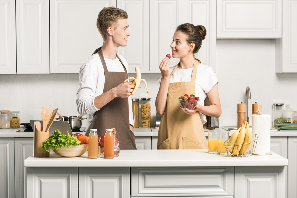 young couple eating healthy fruits and looking at each other in kitchen - Photo, Image