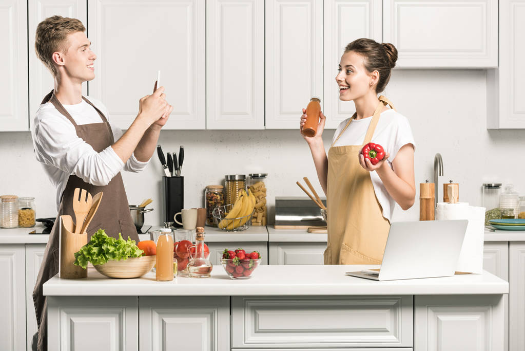хлопець фотографує зі смартфоном дівчини на кухні
 - Фото, зображення