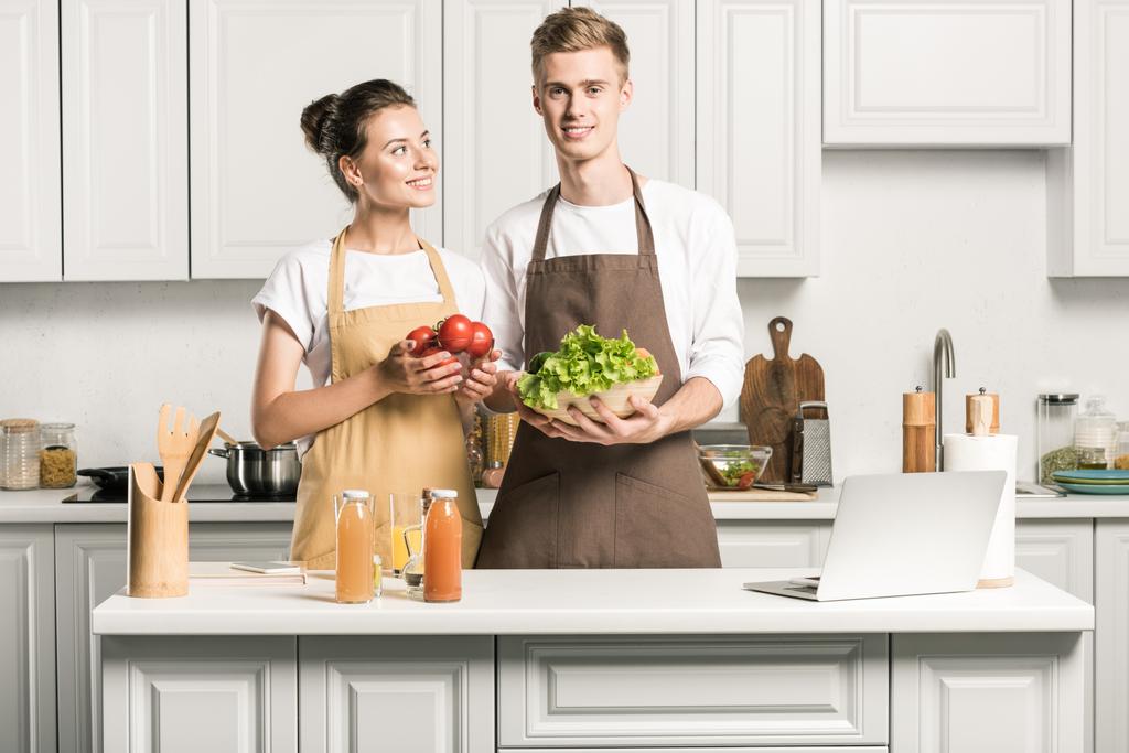 νεαρό ζευγάρι μαγείρεμα σαλάτα και στέκεται με λαχανικά στην κουζίνα - Φωτογραφία, εικόνα