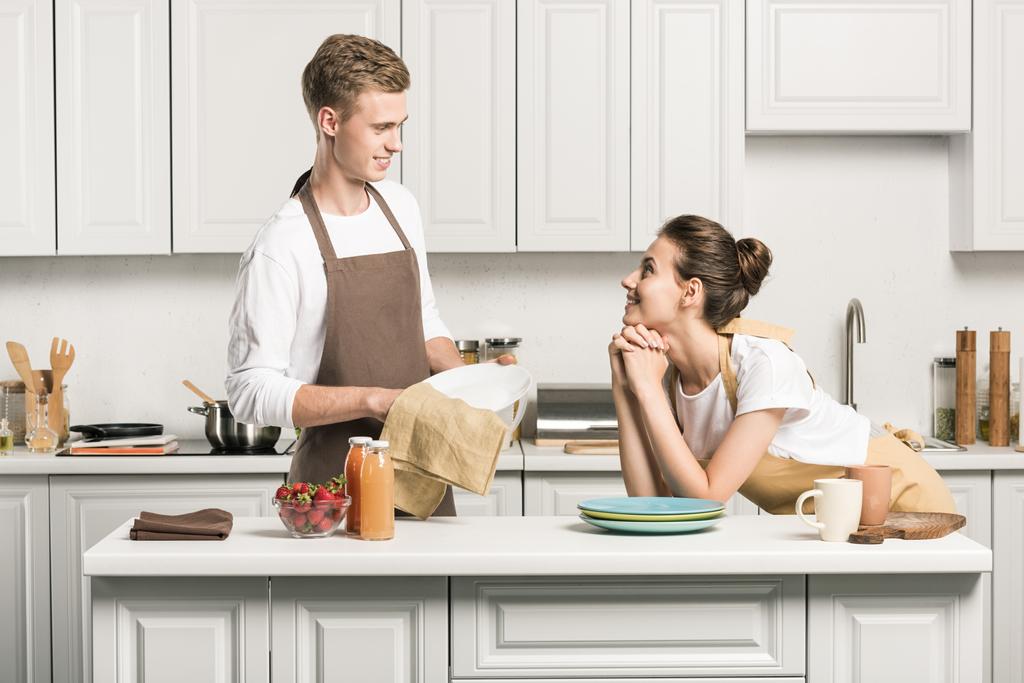 彼氏が見ている彼のガール フレンドのキッチンで料理を乾燥させる - 写真・画像