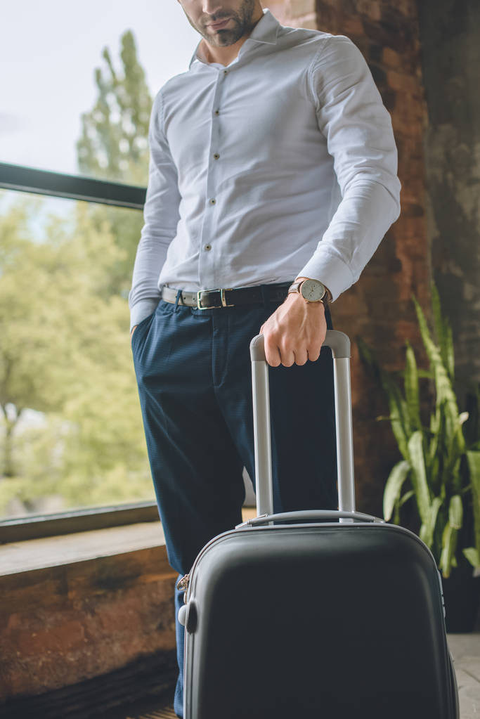 abgeschnittenes Bild eines männlichen Touristen, der mit Koffer zu Hause steht  - Foto, Bild