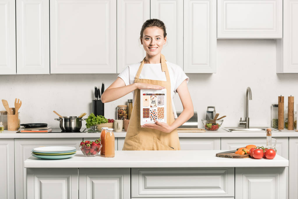 привлекательная девушка держит планшет с загруженной странице pinterest на кухне
 - Фото, изображение