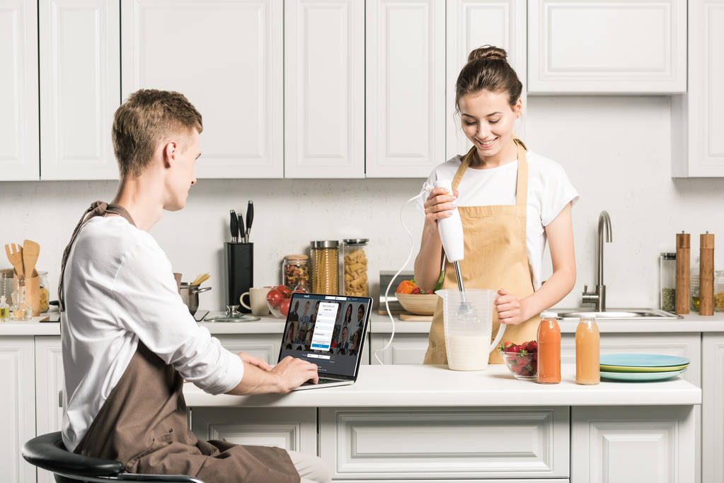 pişirme kız ve erkek arkadaşı dizüstü yüklü LinkedIn sayfa mutfak ile kullanma - Fotoğraf, Görsel