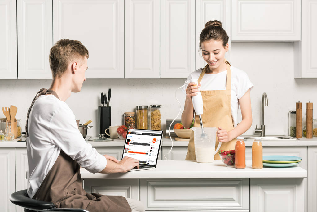 novia cocina y novio usando el ordenador portátil con la página de soundcloud cargado en la cocina
 - Foto, imagen