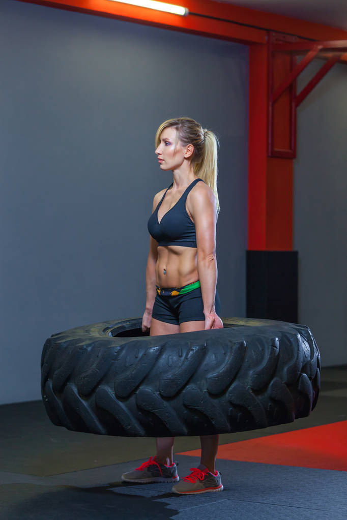 Ajustez athlète féminine travaillant avec un énorme pneu, tournant et porter dans la salle de gym. Crossfit femme exercice avec gros pneu
 - Photo, image