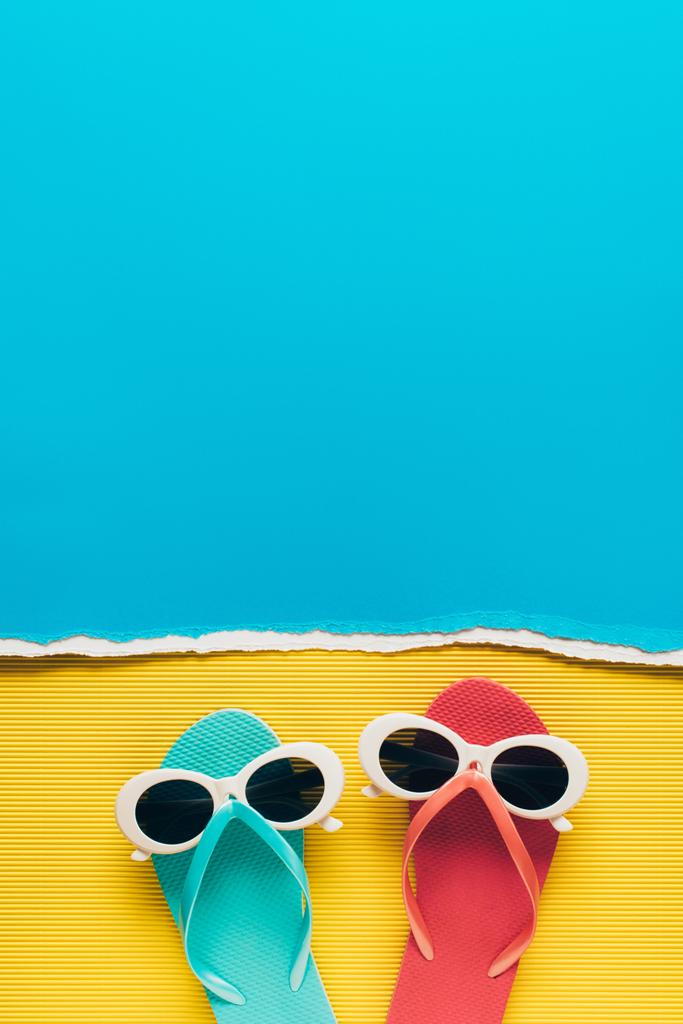 pohled shora z modré a růžové žabky s sluneční brýle na žluté a modré papírové pozadí - Fotografie, Obrázek