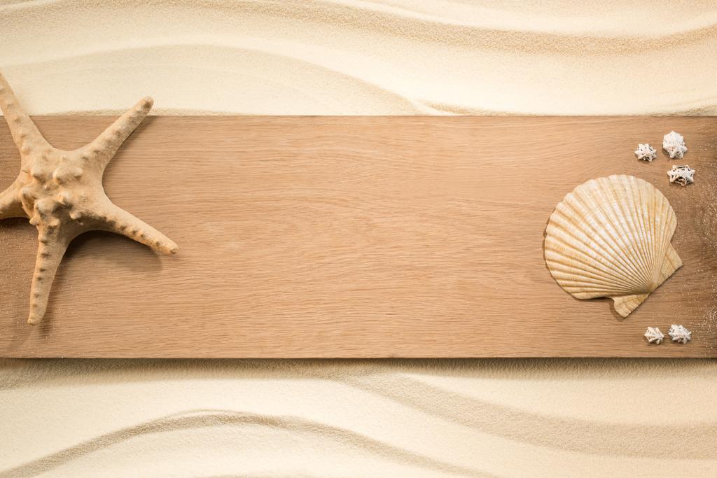 Плоская лежала с расположением морской звезды и морей на деревянной доске на песке
 - Фото, изображение