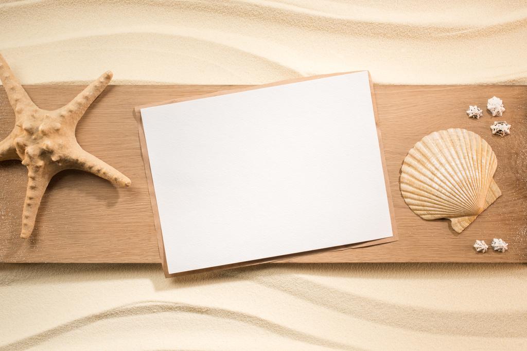 flache Lage mit Blankopapier, Seestern und Muscheln auf Holzplanke auf Sand - Foto, Bild