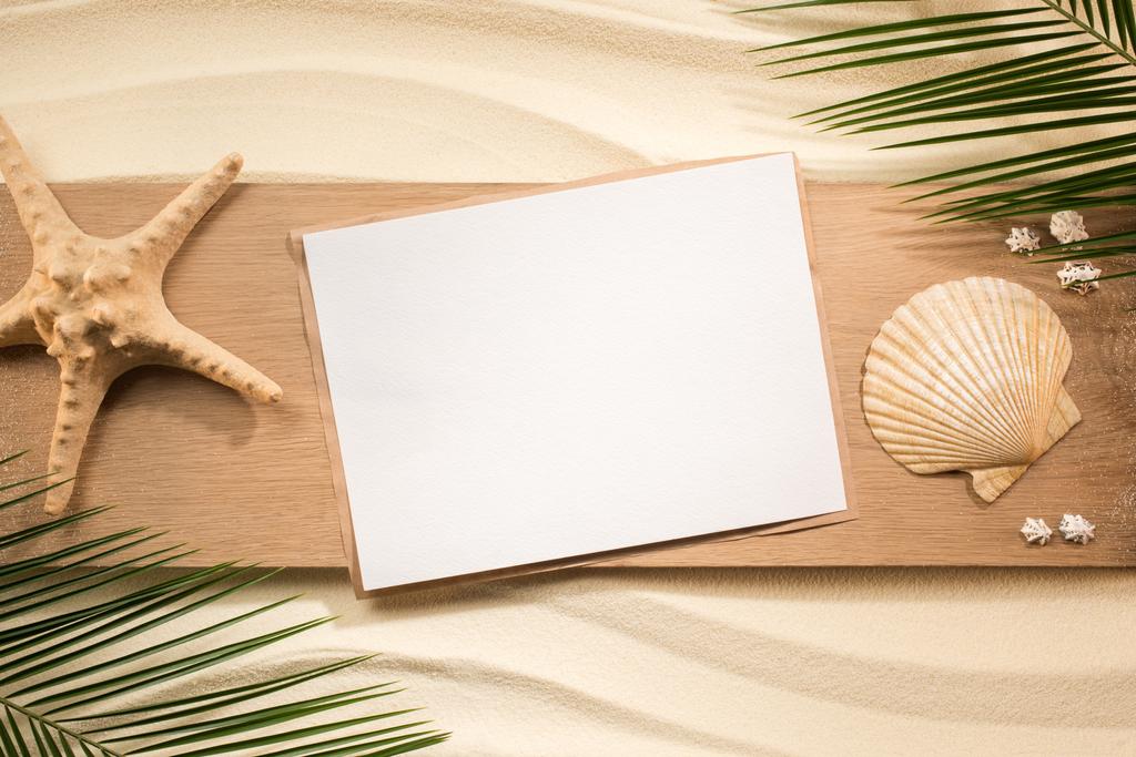 tendido plano con hojas de palma, papel en blanco, estrella de mar y conchas marinas sobre tabla de madera sobre arena
 - Foto, Imagen