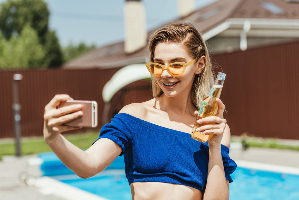 menina atraente feliz levando selfie com garrafa de cerveja no smartphone
 - Foto, Imagem