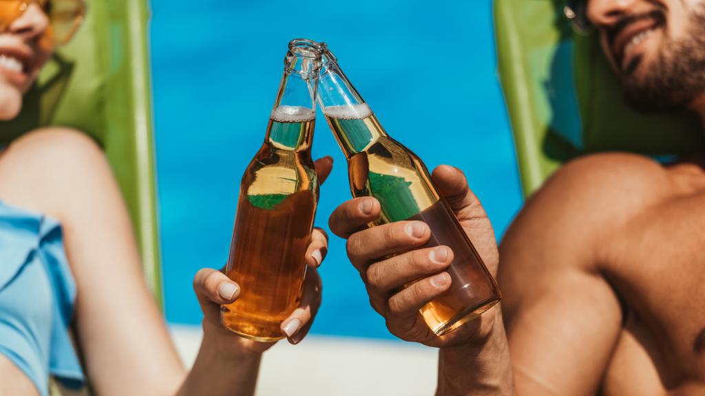 vista recortada de pareja tintineo con botellas de cerveza en tumbonas
 - Foto, imagen