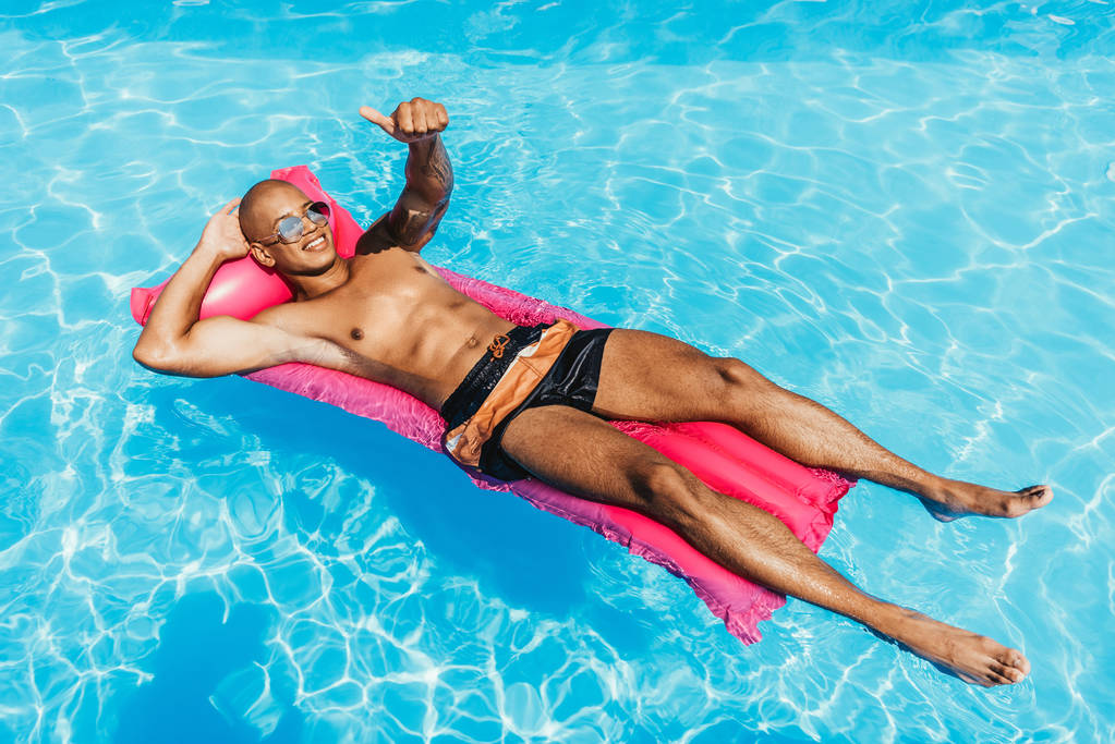 homme afro-américain montrant pouce levé tout en bronzant sur matelas gonflable dans la piscine
 - Photo, image