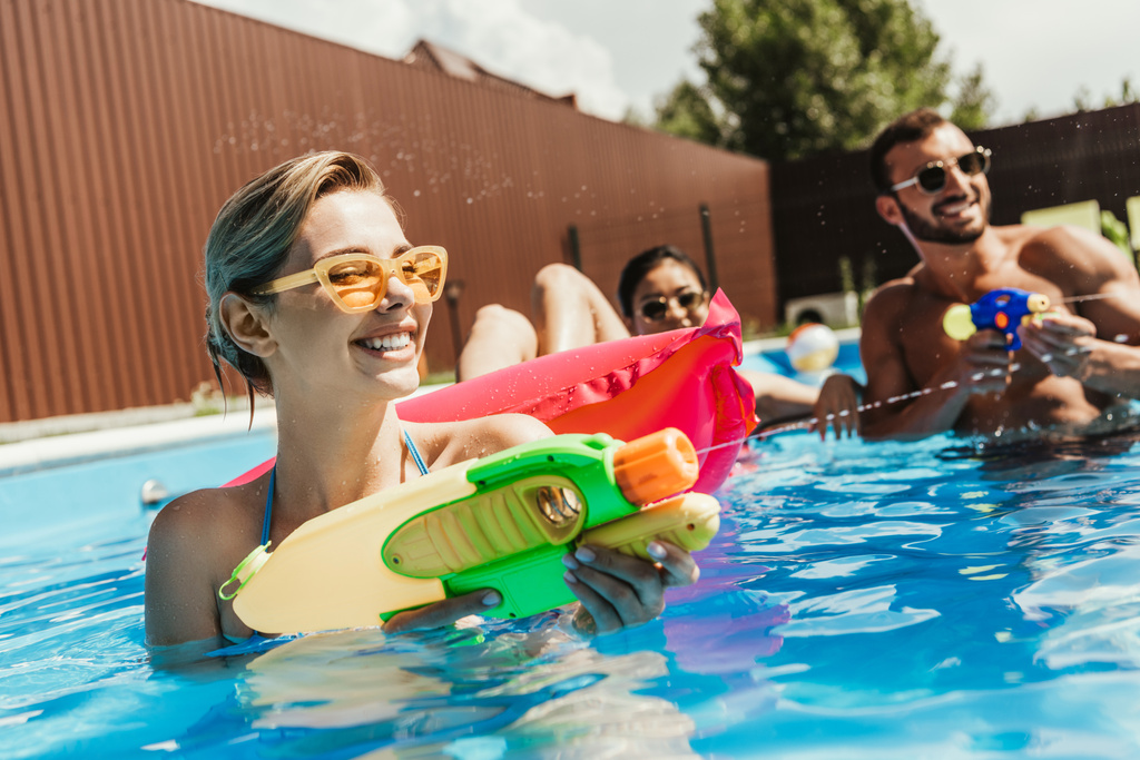 fröhliche multiethnische Freunde spielen mit Wasserpistolen im Schwimmbad - Foto, Bild