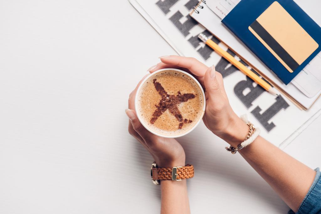 foto recortada de la mujer sosteniendo la taza de café con el cartel de avión en la mesa con tarjeta de crédito, pasaporte y billete, concepto de viaje
 - Foto, imagen