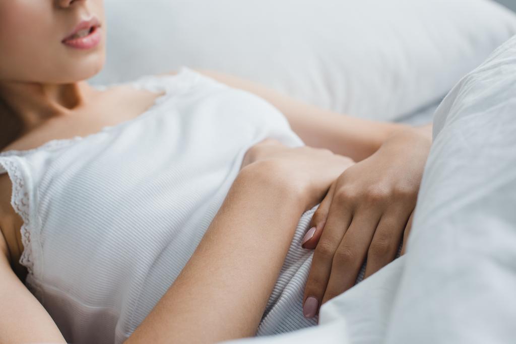 colpo ritagliato di giovane donna che soffre di mal di stomaco a letto
 - Foto, immagini