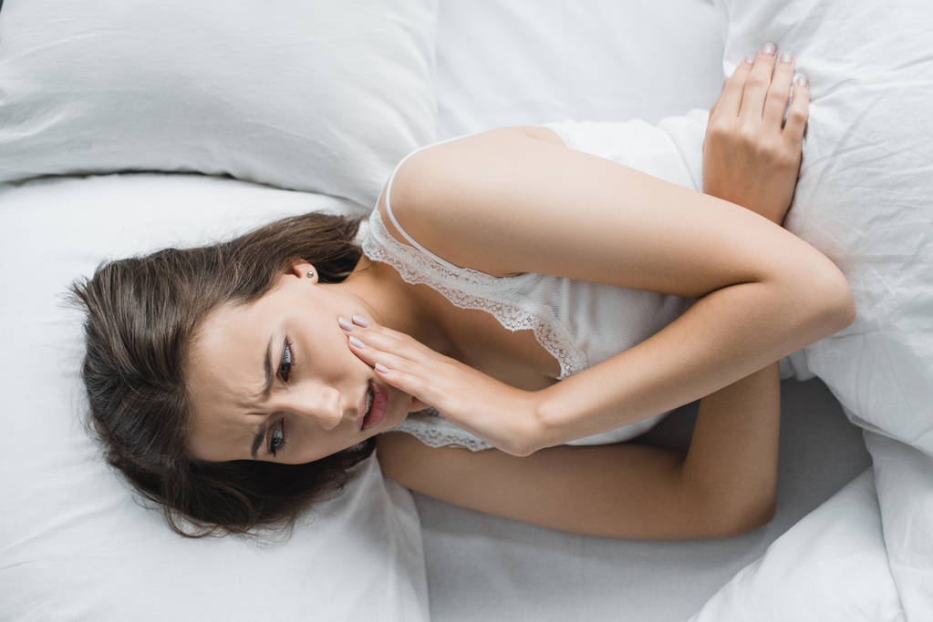 vista superior da jovem mulher que sofre de dor de dente enquanto deitada na cama
  - Foto, Imagem