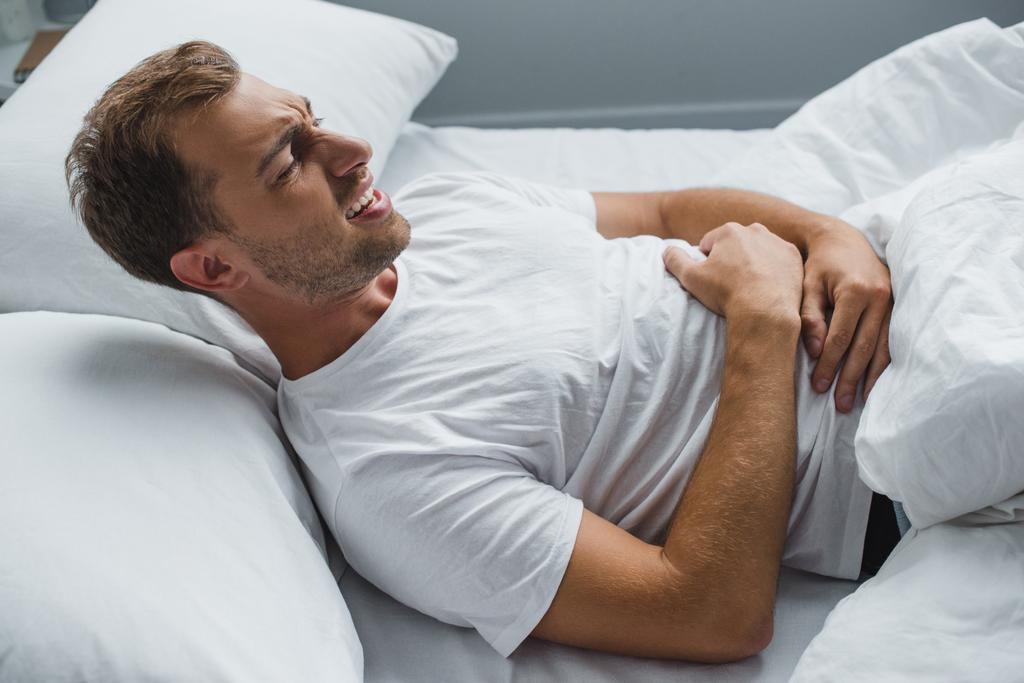 vysoký úhel pohled člověka, ležící v posteli a trpí bolest žaludku  - Fotografie, Obrázek