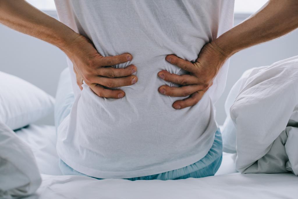 Schnappschuss eines Mannes, der auf dem Bett sitzt und unter Rückenschmerzen leidet - Foto, Bild