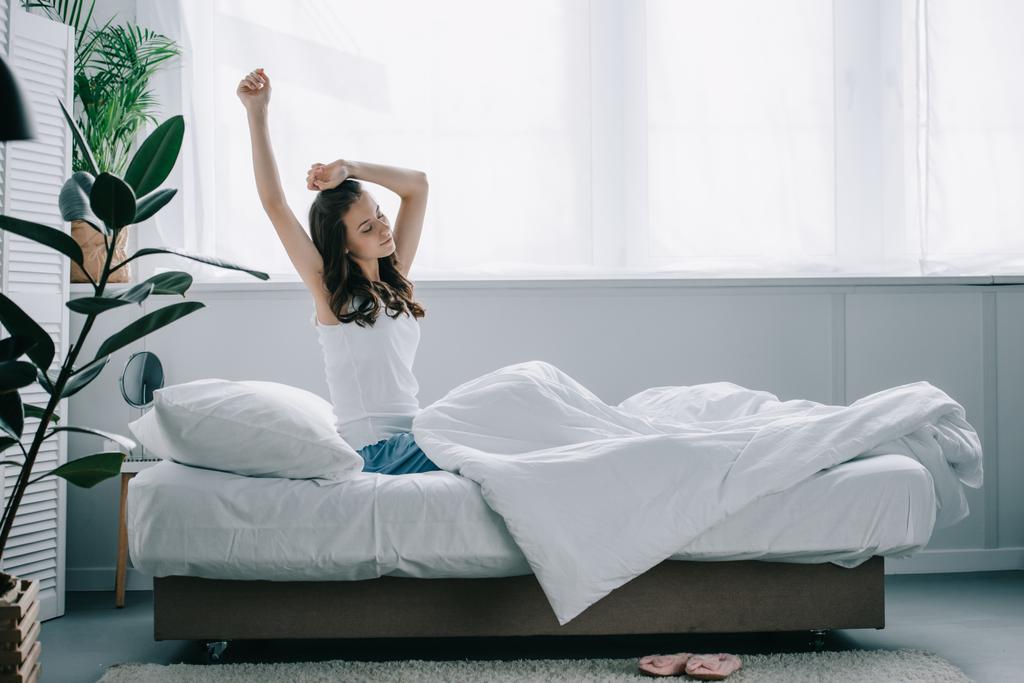 mooie jonge brunette vrouw uitrekken op bed in de ochtend - Foto, afbeelding