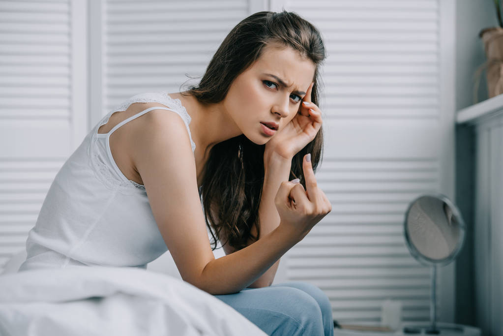 young woman with headache giving the finger and looking at camera in bedroom - Photo, Image