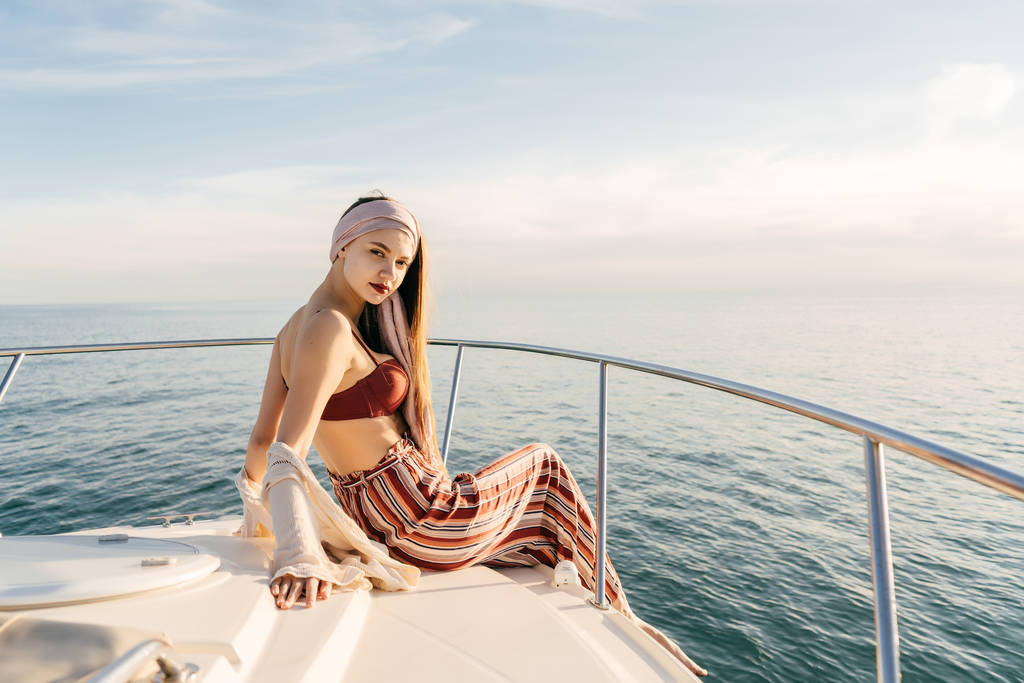 tyylikäs tyttö muodikkaissa kesävaatteissa istuu valkoisella jahdilla, purjehtii Karibian merellä, kauan odotettu loma.
 - Valokuva, kuva
