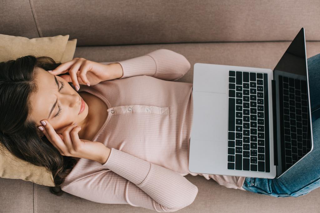 Draufsicht auf junge Frau mit Kopfschmerzen mit Laptop mit leerem Bildschirm zu Hause - Foto, Bild