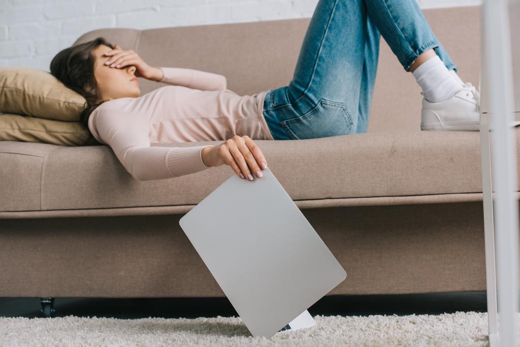 Młoda kobieta o ból głowy i ból w oczach, leżąc na kanapie i trzymając laptop - Zdjęcie, obraz