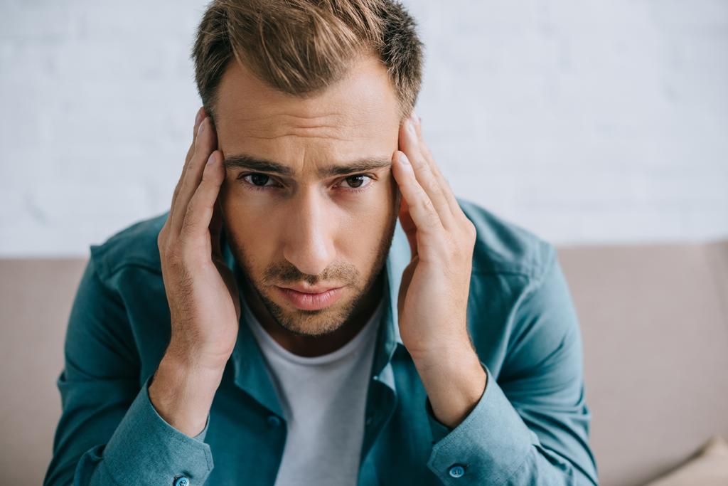 young man with headache looking at camera while sitting at home  - Photo, Image